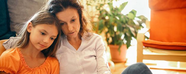 A mother and her young daughter sitting together indoors, looking intently at something off-camera with a focused and warm expression.