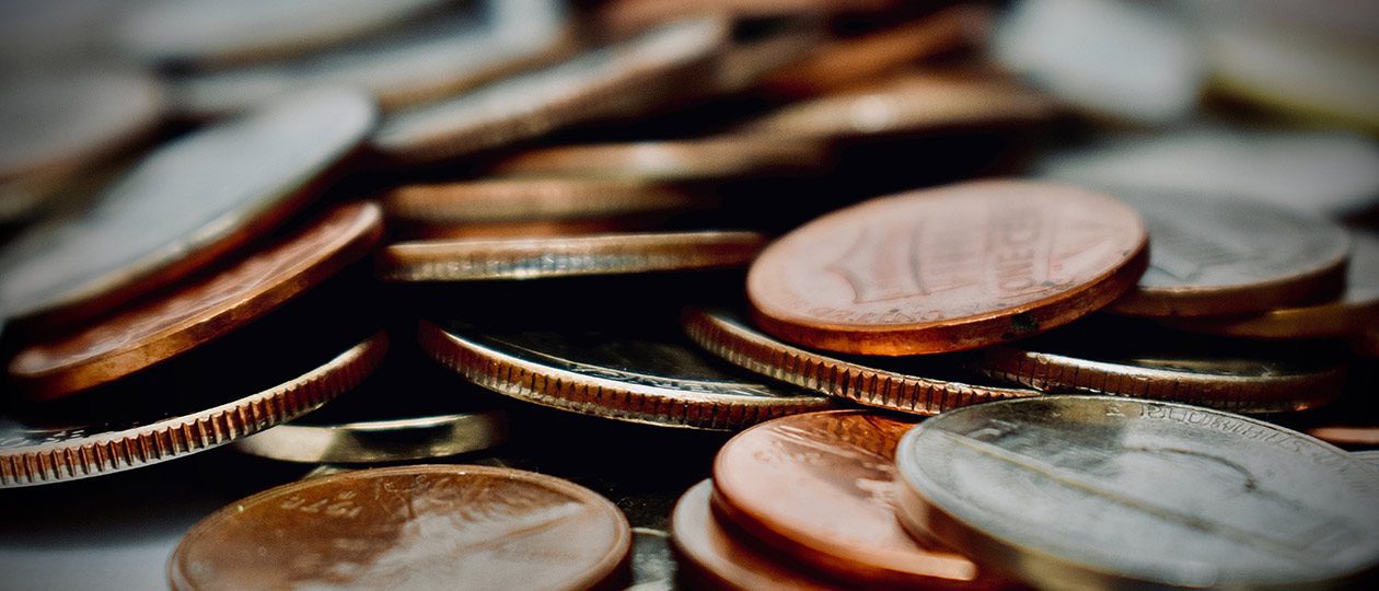 Close-up, shallow-depth-of-field shot of a pile of assorted copper and silver coins on a dark surface.
