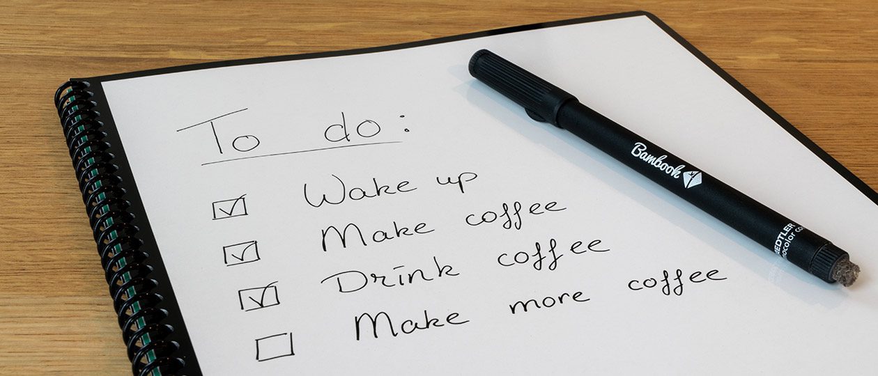 A spiral notebook with a handwritten "To do" list and checkmarks next to a black pen.