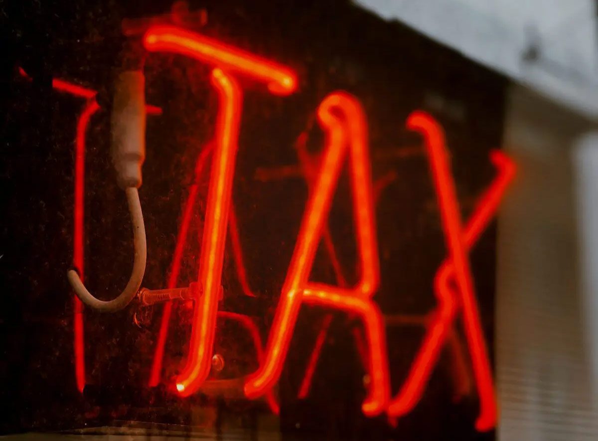 A glowing red neon sign that spells out the word "TAX" in bright, stylized letters against a dark background.