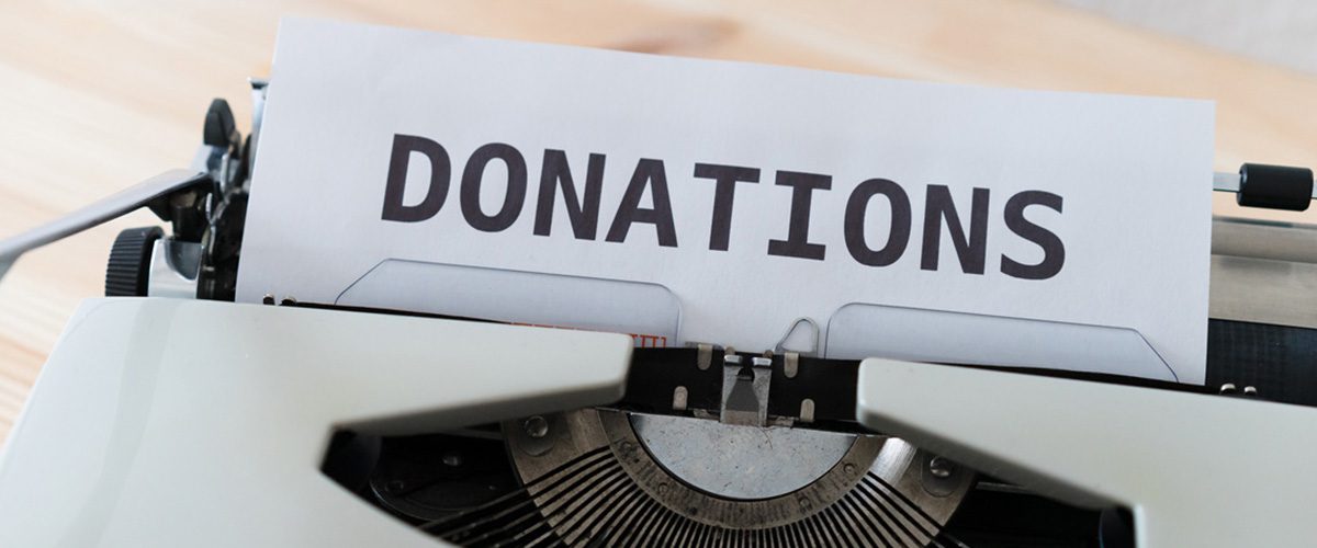 Close-up of a vintage white typewriter with a piece of paper that has the word "DONATIONS" printed in bold black letters.