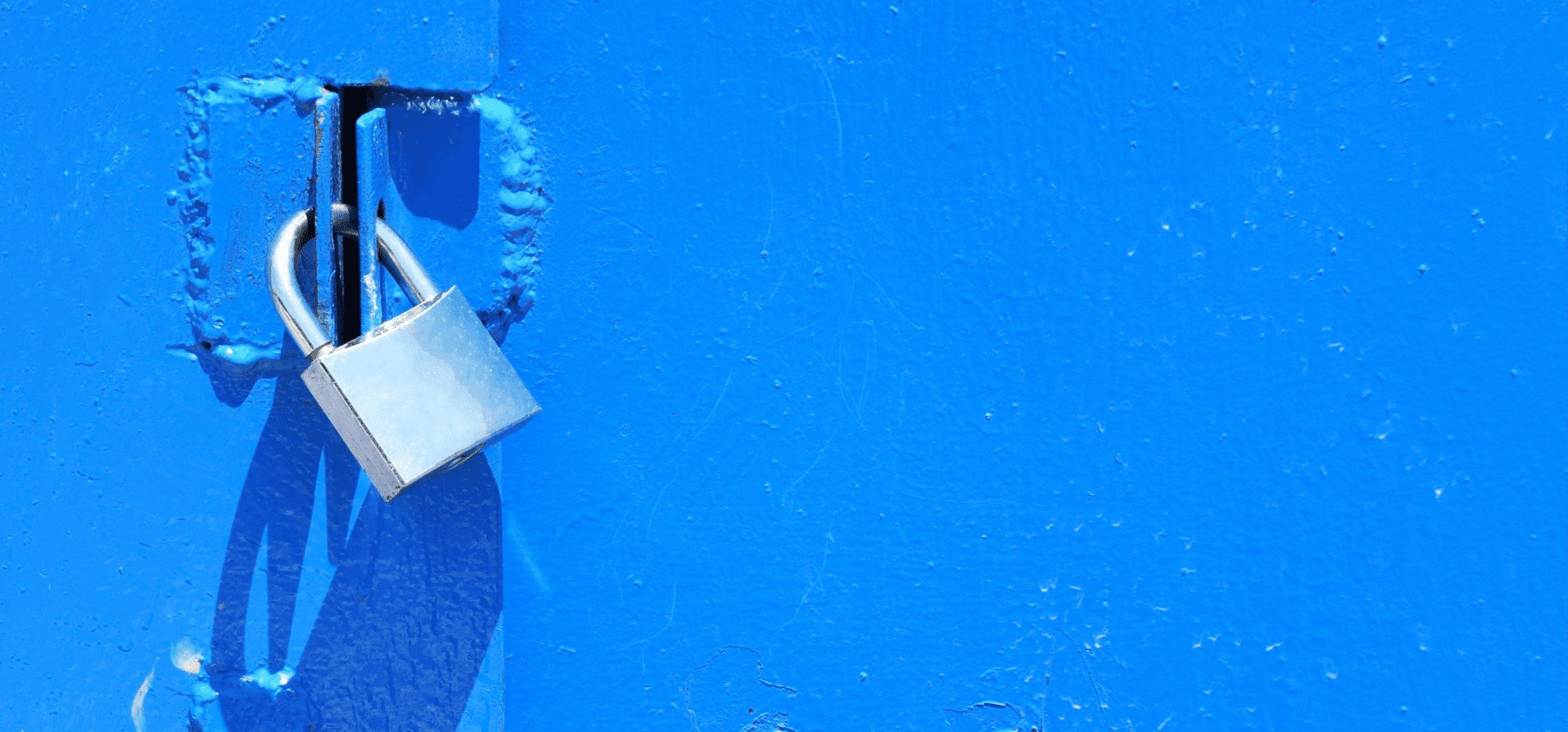 A silver padlock secured to a bright blue metal door, symbolizing financial security and account protection.
