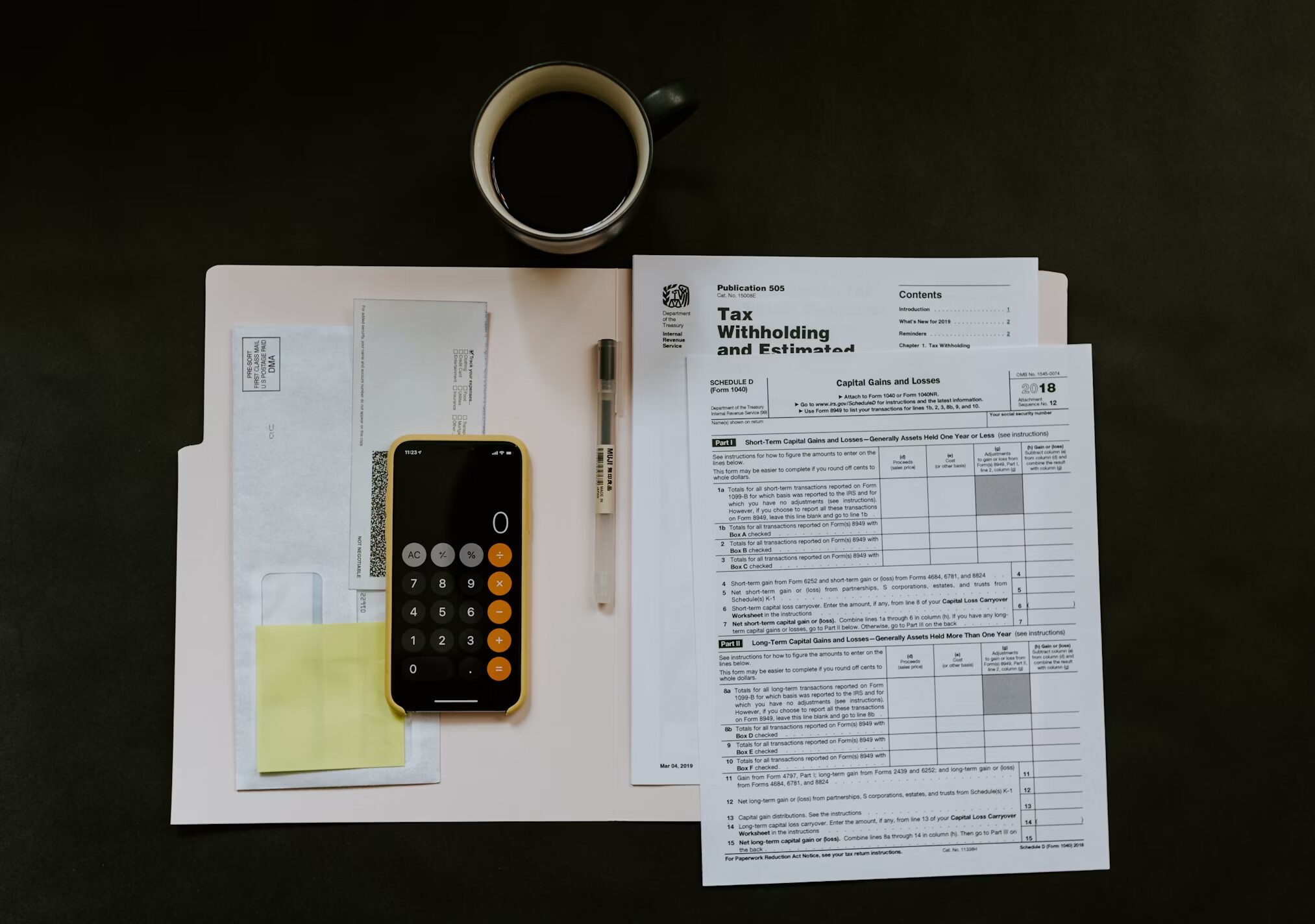 Top-down view of an IRS tax form for Capital Gains and Losses, a calculator on a smartphone, and a cup of black coffee on a dark desk.