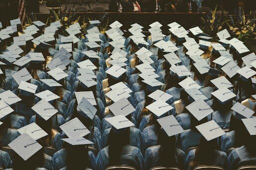 A high-angle view of several rows of graduates wearing white and blue academic caps during a commencement ceremony.