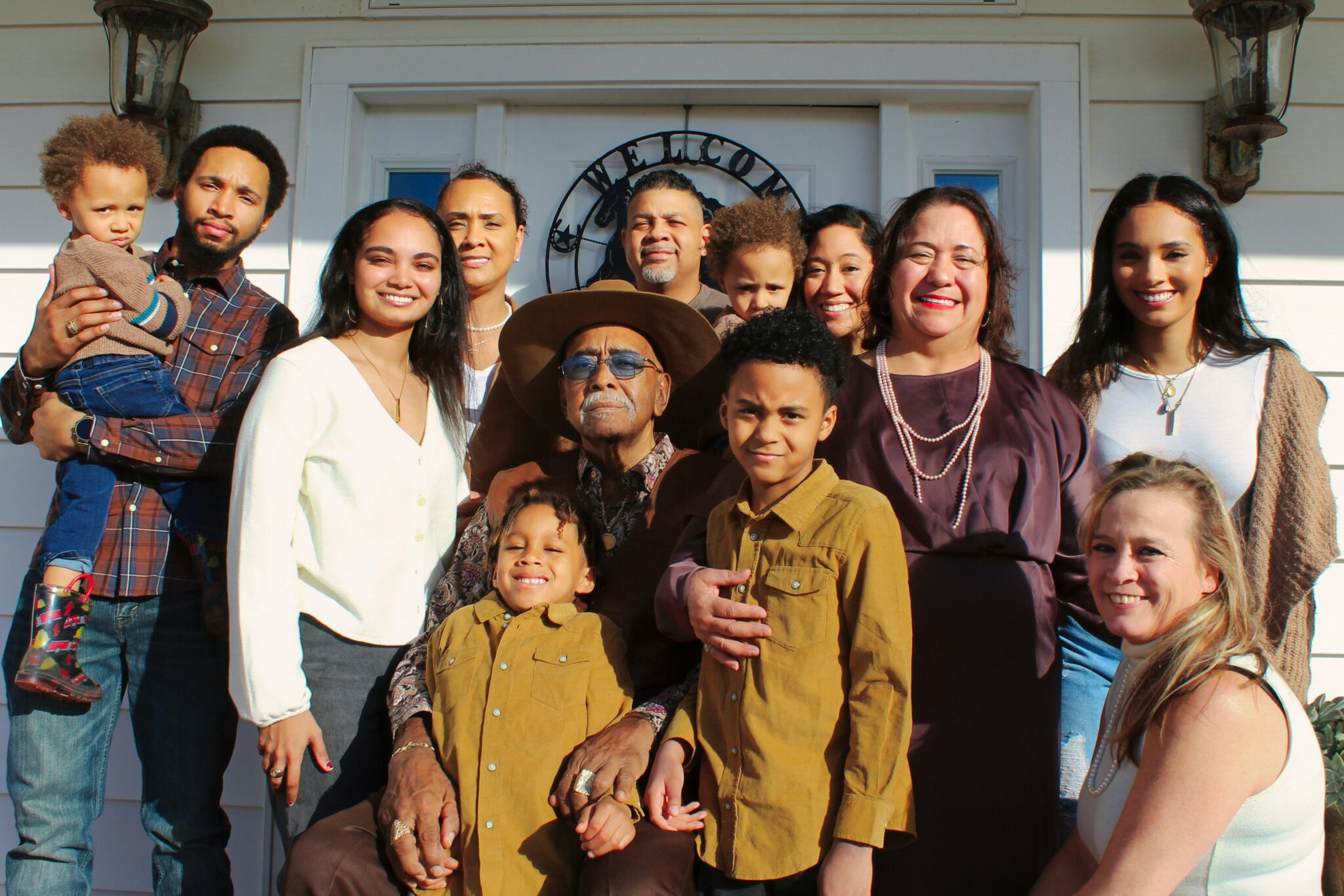 A large, diverse multi-generational family smiling together on a front porch.