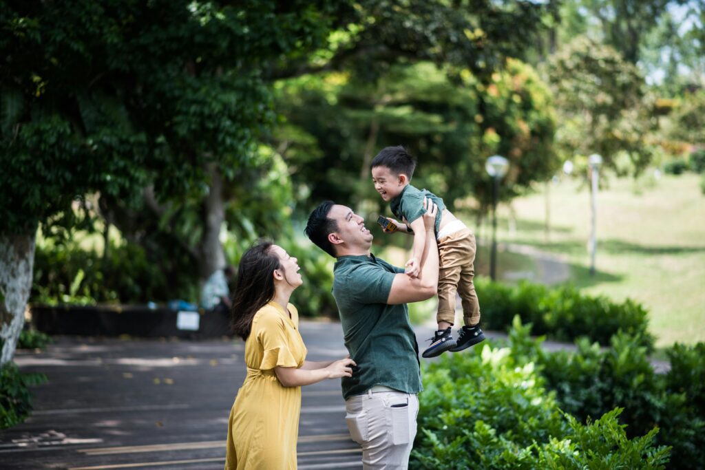 Father playing with and lifting his child up in a sunlit park.