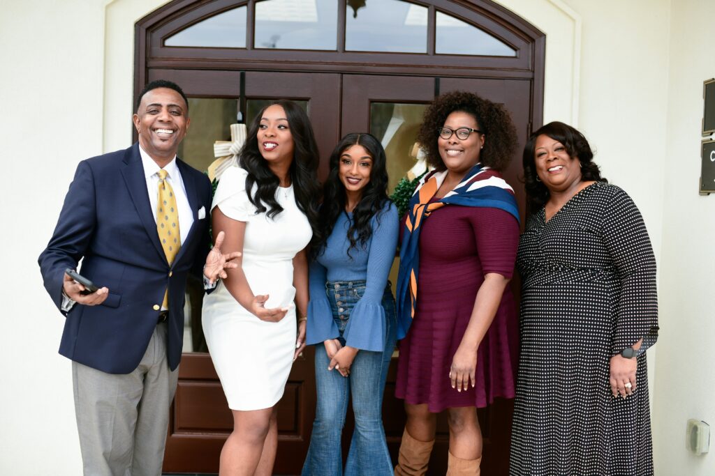 A smiling, well-dressed family standing together outside a house front door.