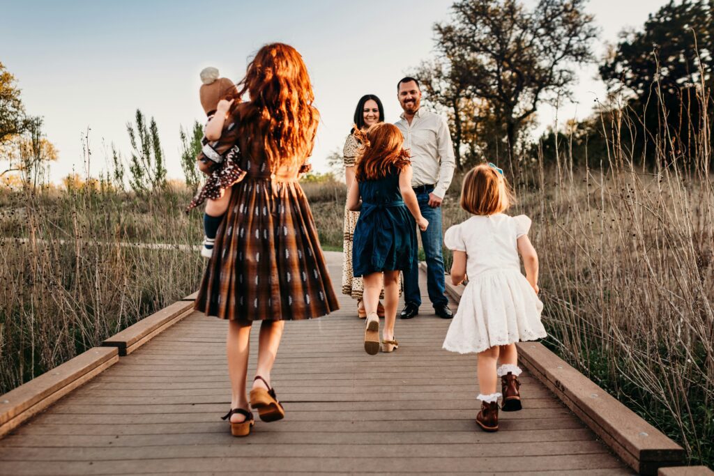"A family with young children walking together down a wooden path in an outdoor field.
