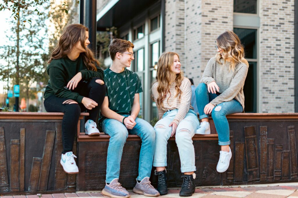 Four people sitting on a ledge of an urban outdoor area, talking and interacting while holding various items.