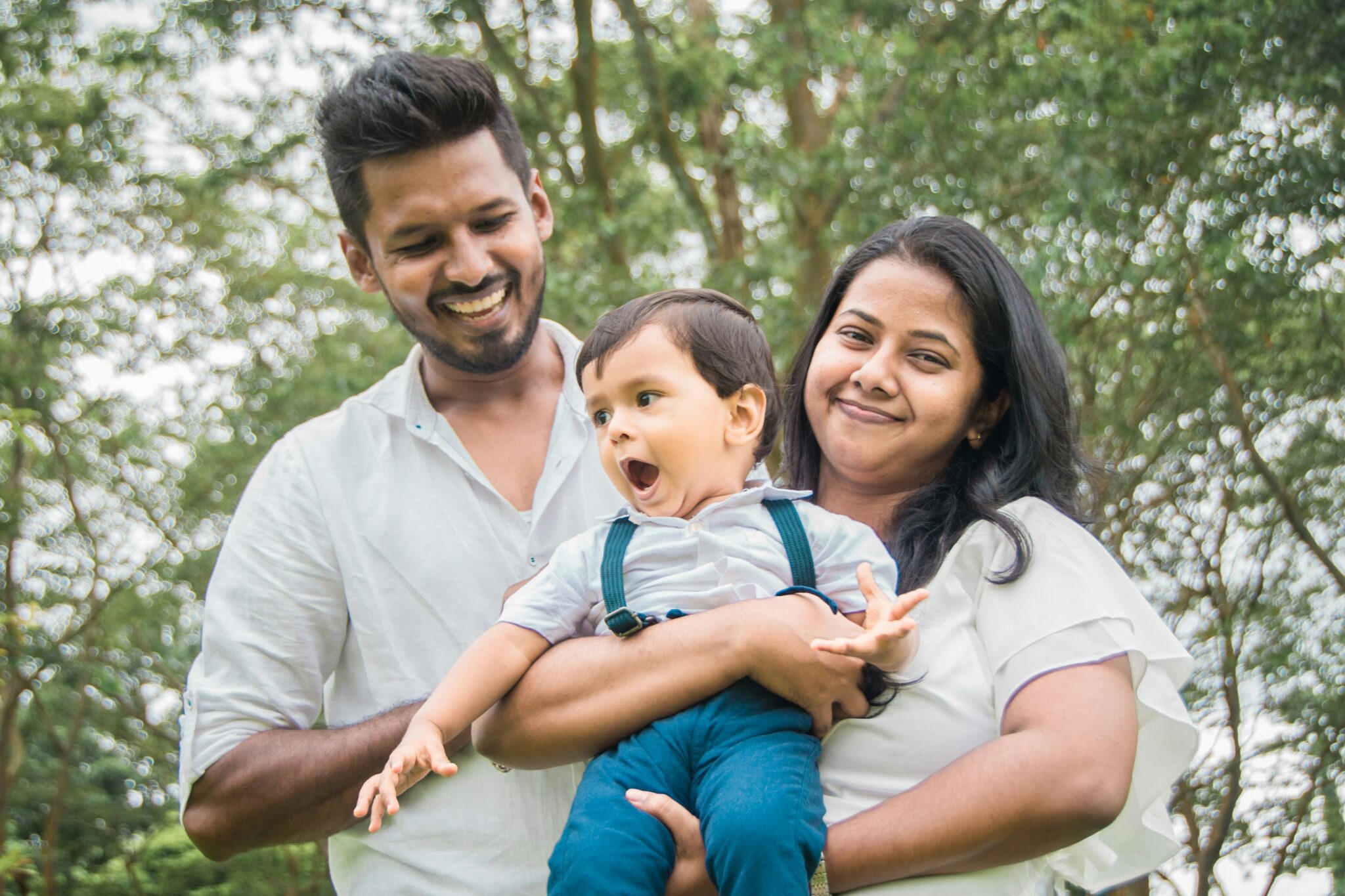 Young parents holding their child while sitting together outdoors in a park, illustrating early family financial planning and legacy