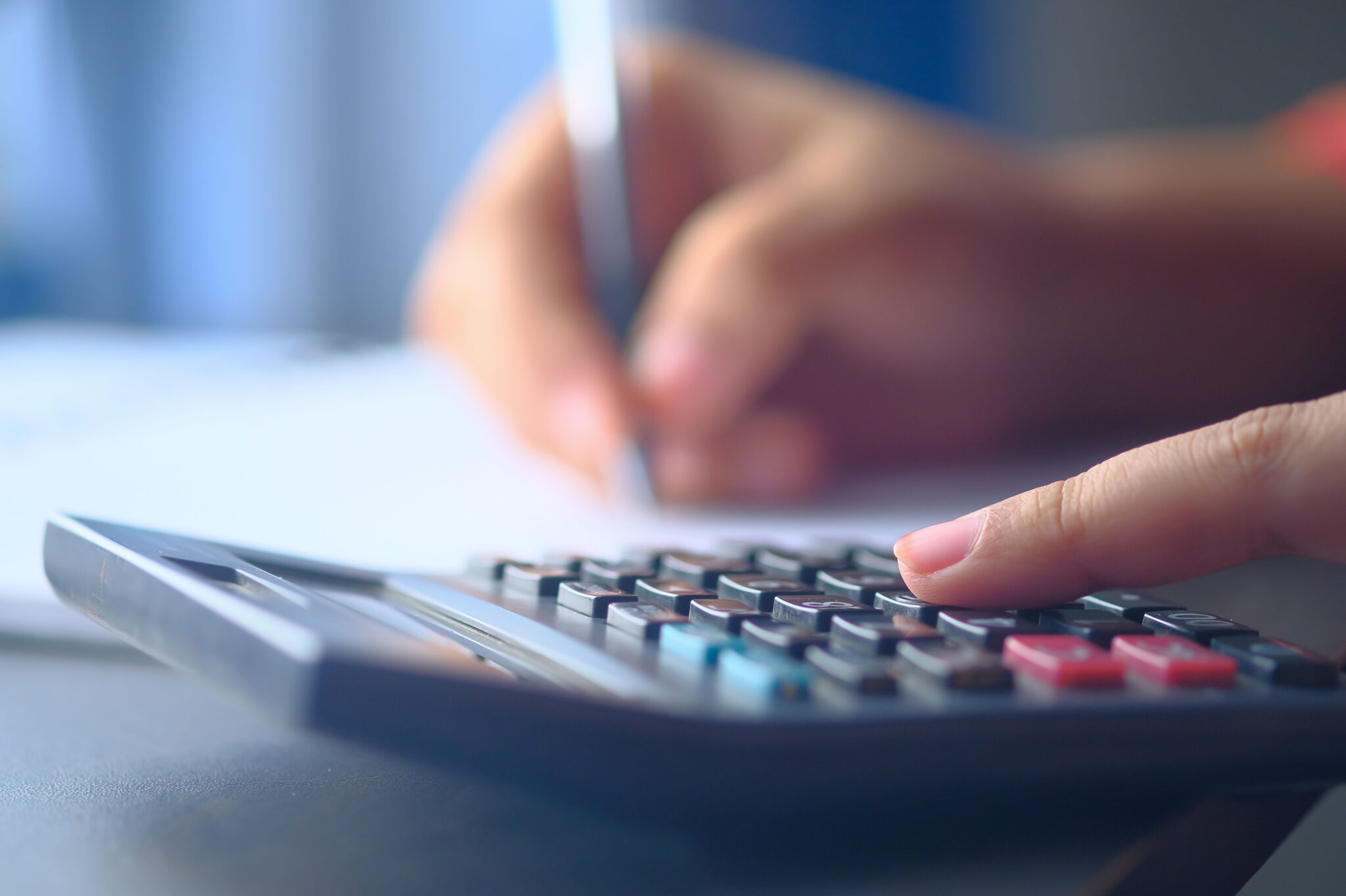 Close-up of a person using a calculator while holding a pen to take notes on paper.