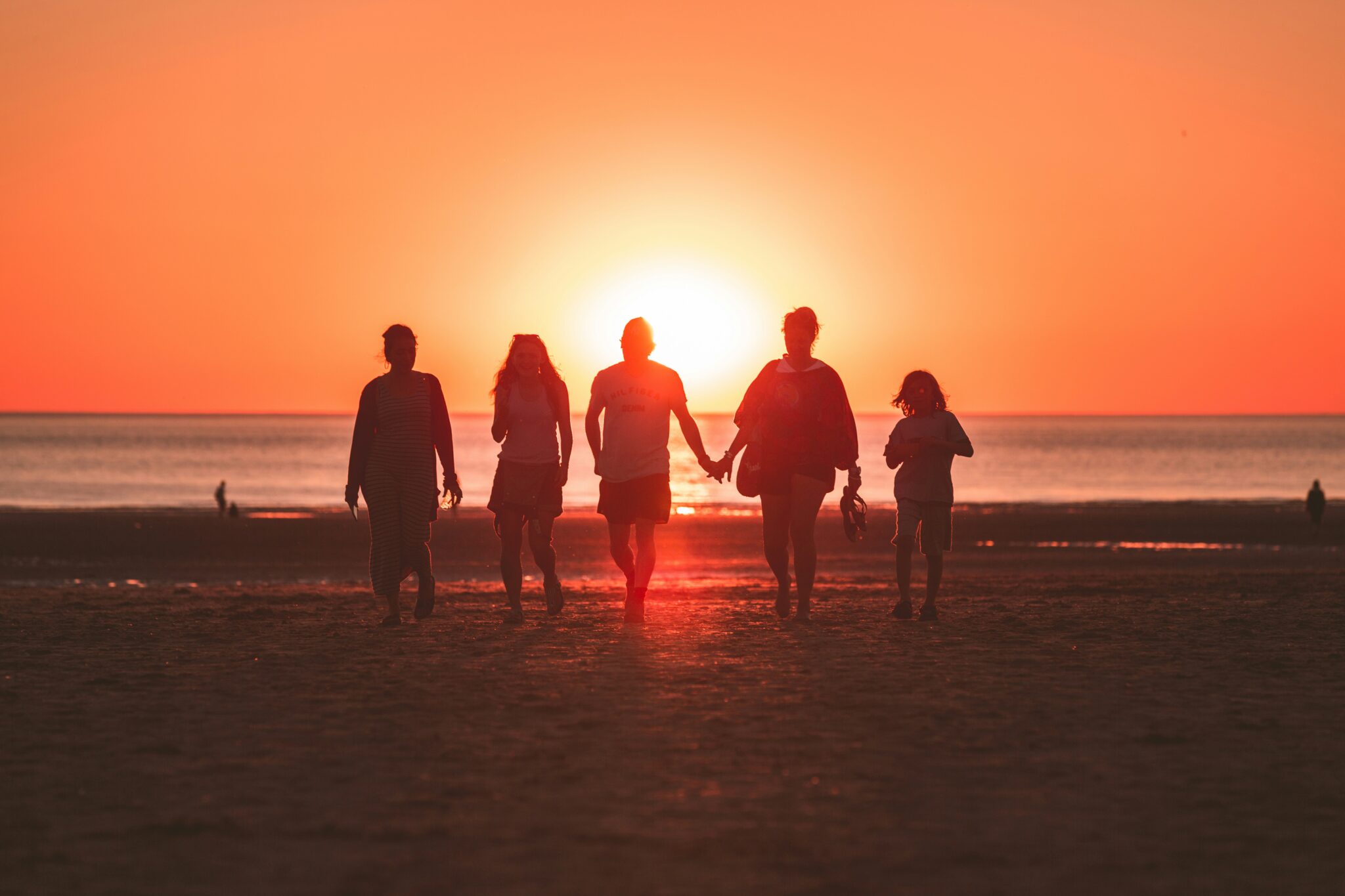 Silhouette of a family of five holding hands while walking on a beach during a golden sunset.